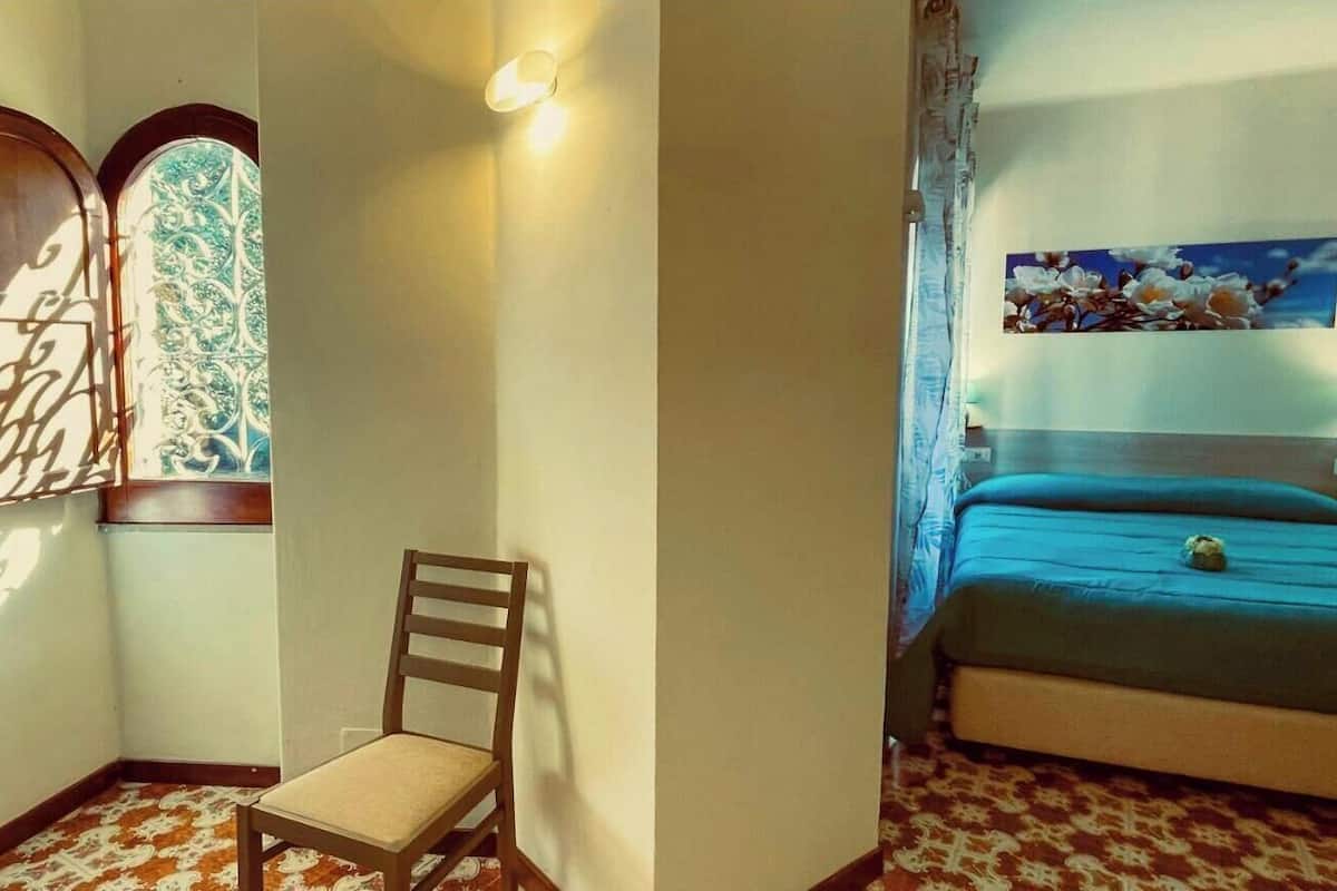 Una habitación con una cama, una silla, una lámpara de pared y un ventanal decorativo.