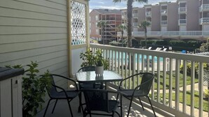 Ein Balkon mit Glastisch und Stühlen, einem Blumentopf und Blick auf einen Swimmingpool sowie Gebäude im Hintergrund.