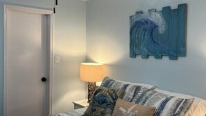 Ein Schlafzimmer mit einem Bett, einem Deckenventilator, einem Wandbild und einem Nachttisch mit Lampe.