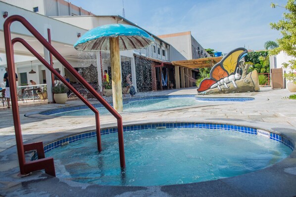 A swimming pool with a blue-tiled edge, a red metal ladder, and a water fountain. - Pousada Cunha (Caldas Novas)