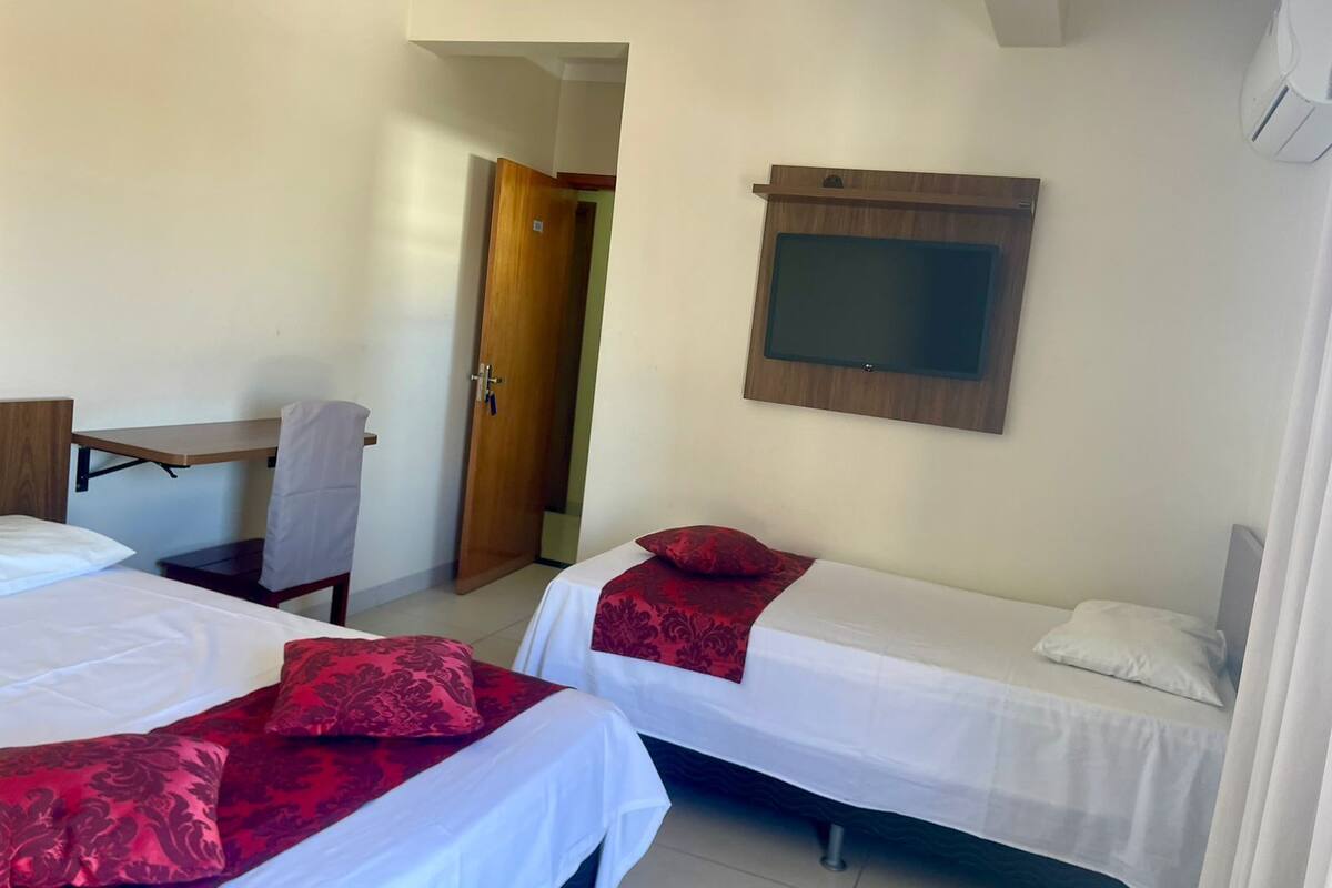 A hotel room with two beds, a desk, a chair, and a TV mounted on the wall.