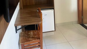 A compact room with a wooden cabinet, a small white refrigerator, and a wooden chair. - Pousada Cunha (Caldas Novas)