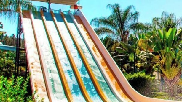 A water slide with multiple lanes, surrounded by greenery and a clear sky. - Pousada Cunha (Caldas Novas)