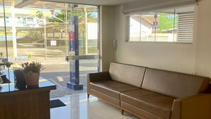 A reception area with a wooden desk, a brown leather sofa, and a large window with blinds. - Pousada Cunha (Caldas Novas)