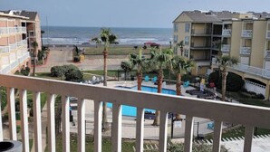 A balcony with a view of a pool, palm trees, and a beach. - Isle B Back Seawall Gulf & Pool View! Come Chillax (Galveston)