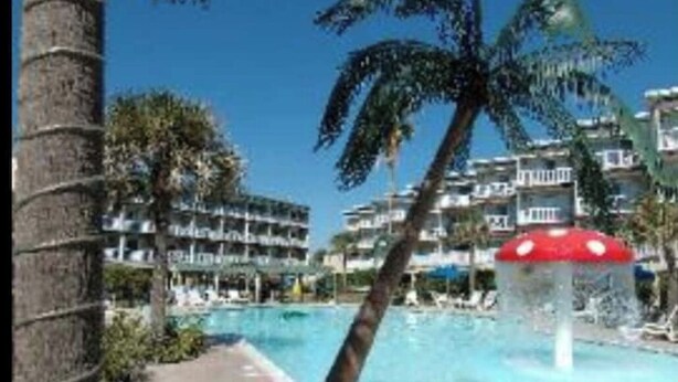 A swimming pool with palm trees and a building in the background. - Isle B Back Seawall Gulf & Pool View! Come Chillax (Galveston)