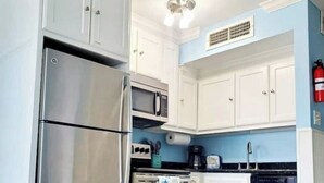 A kitchen with stainless steel appliances, white cabinets, and a blue accent wall. - Beach Escape Seawall View 2 Pool (Galveston)