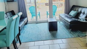 A living room with a sofa, a coffee table, and a TV. There are chairs and a balcony with a view. - Beach Escape Seawall View 2 Pool (Galveston)