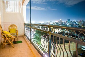 Un balcone con ringhiera in metallo curvo, vista sulla città al crepuscolo e due poltrone in vimini con cuscini.