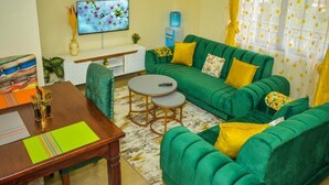 Una sala de estar con un sofá verde, una mesa de centro de madera y un televisor en la pared.