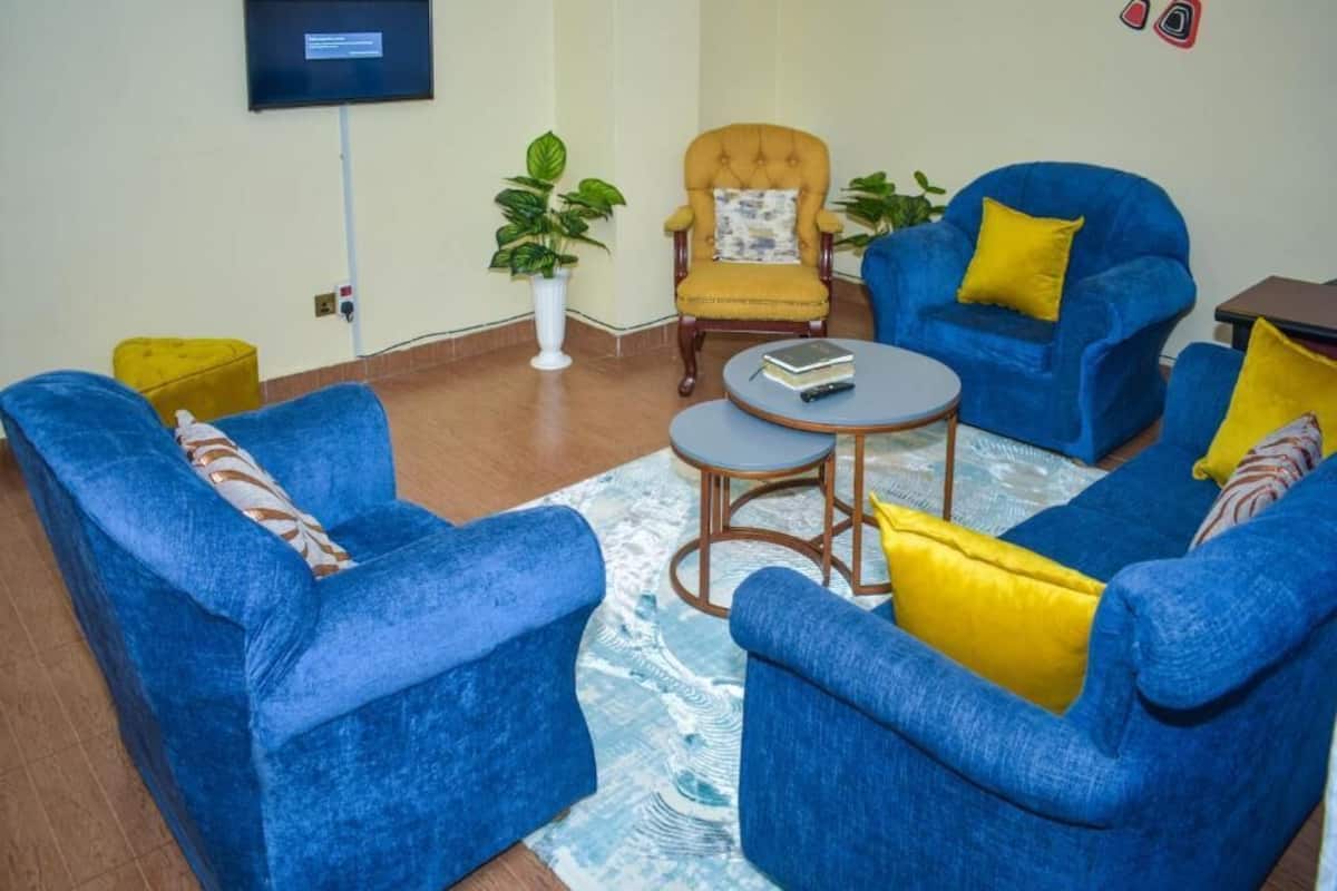 Una sala de estar con sofás azules, un sillón amarillo y una mesa de centro redonda.