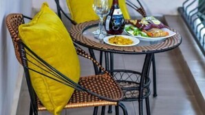 Un rincón de comedor con sillas de mimbre y cojines amarillos, una mesa redonda con platos de comida, una botella y vasos.