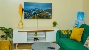 Una sala de estar con sofás verdes, una mesa de centro redonda, un mueble blanco para televisión y un cuadro en la pared.