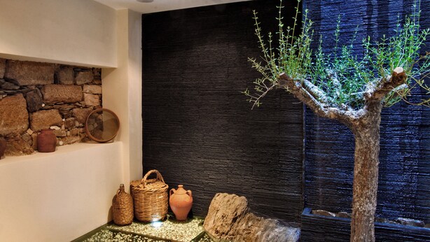 A room with a stone wall, a wooden tree, and various rustic items like baskets and pottery. - Casa dos Poços (Figueira de Castelo Rodrigo)