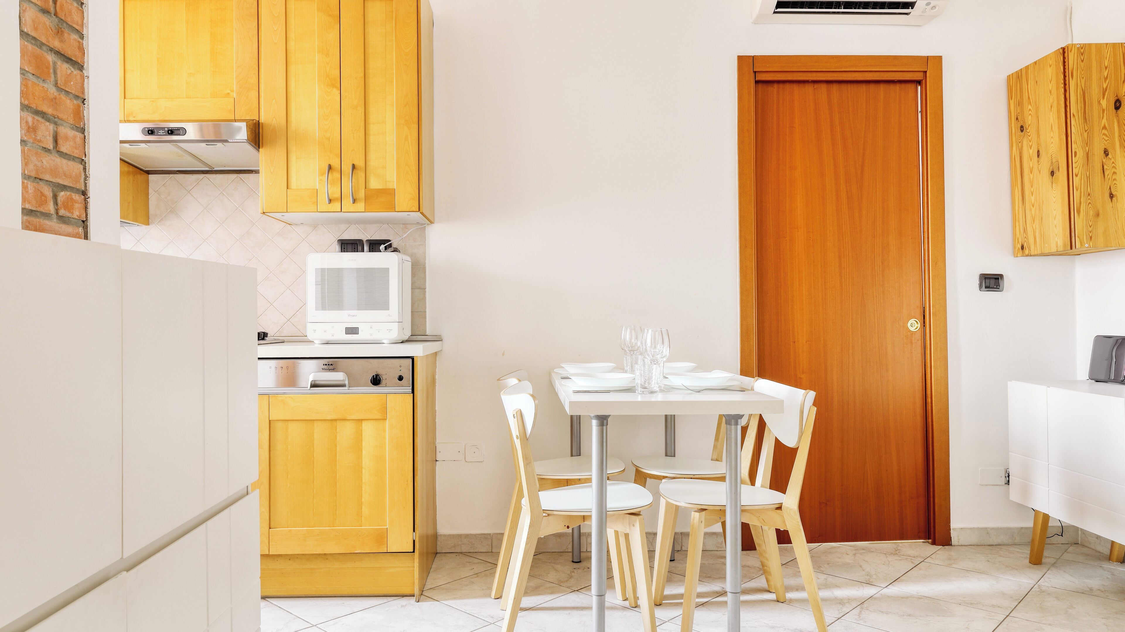 A compact kitchen with wooden cabinets, a built-in microwave, and a dining area with a table and chairs.
