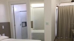 A hotel room with a bed, a door leading to another room, and a bathroom with a shower curtain. - Hotel Primavera (Bom Despacho)