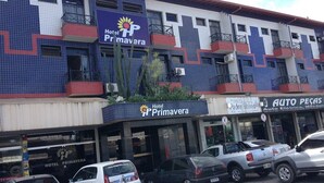 A hotel with a tiled facade, multiple balconies, and a parking lot with several cars. - Hotel Primavera (Bom Despacho)