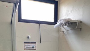 A small bathroom with a toilet, a trash can, a shower, and a window above the toilet. - Hotel Primavera (Bom Despacho)