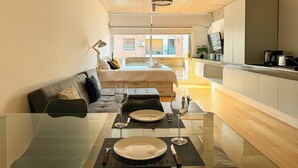 A modern, compact living space with a glass dining table, a sofa, a bed, and a kitchen area. - BT Homes - Palermo, Soler (Buenos Aires)