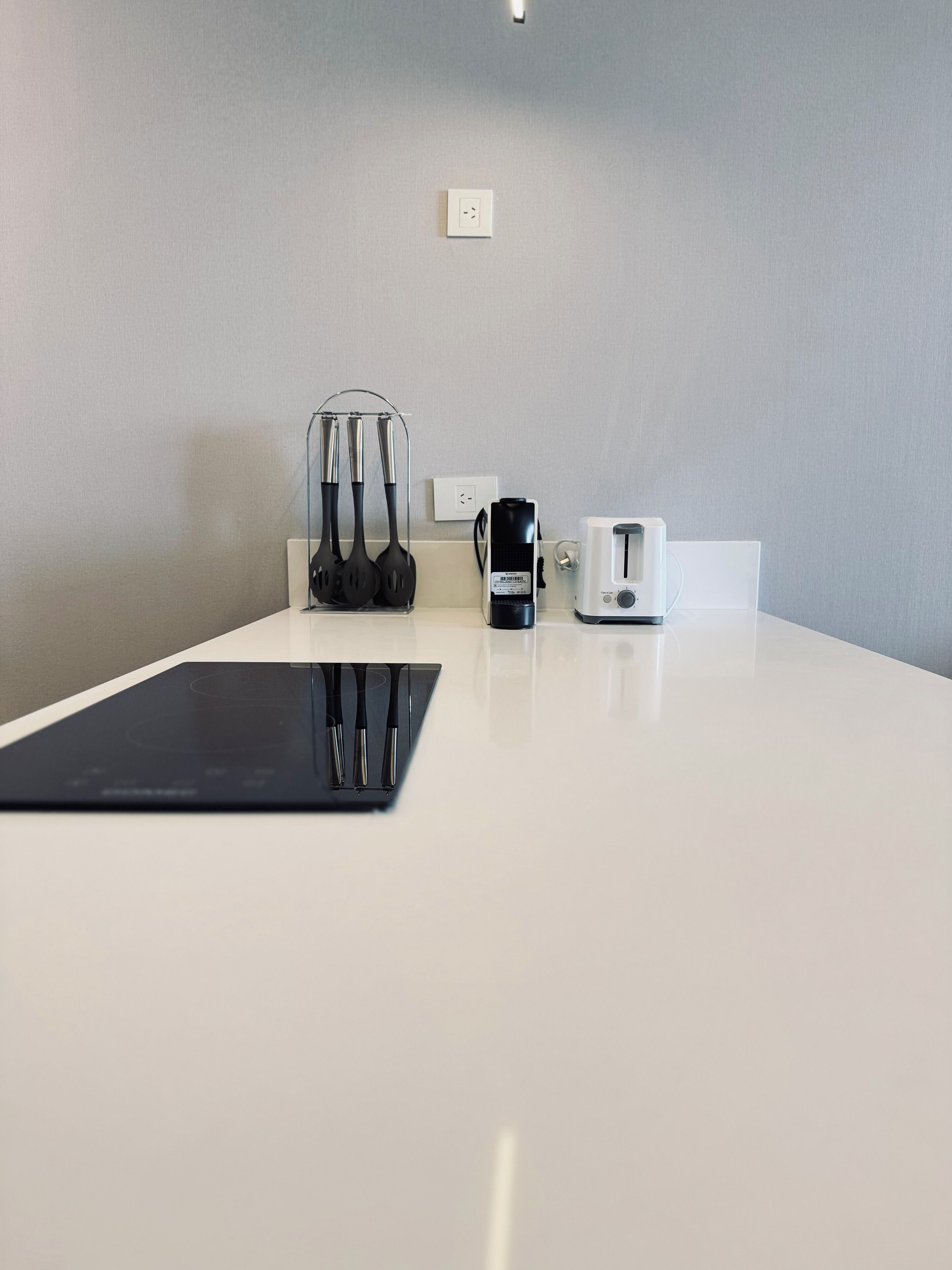 Une table blanche avec une tablette noire, une machine à café et un grille-pain. Il y a une prise de courant au-dessus de la table.