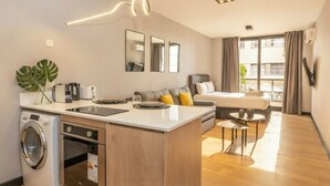 Habitación de hotel pequeña con kitchenette, cama, un rincón para comer y un ventanal grande.