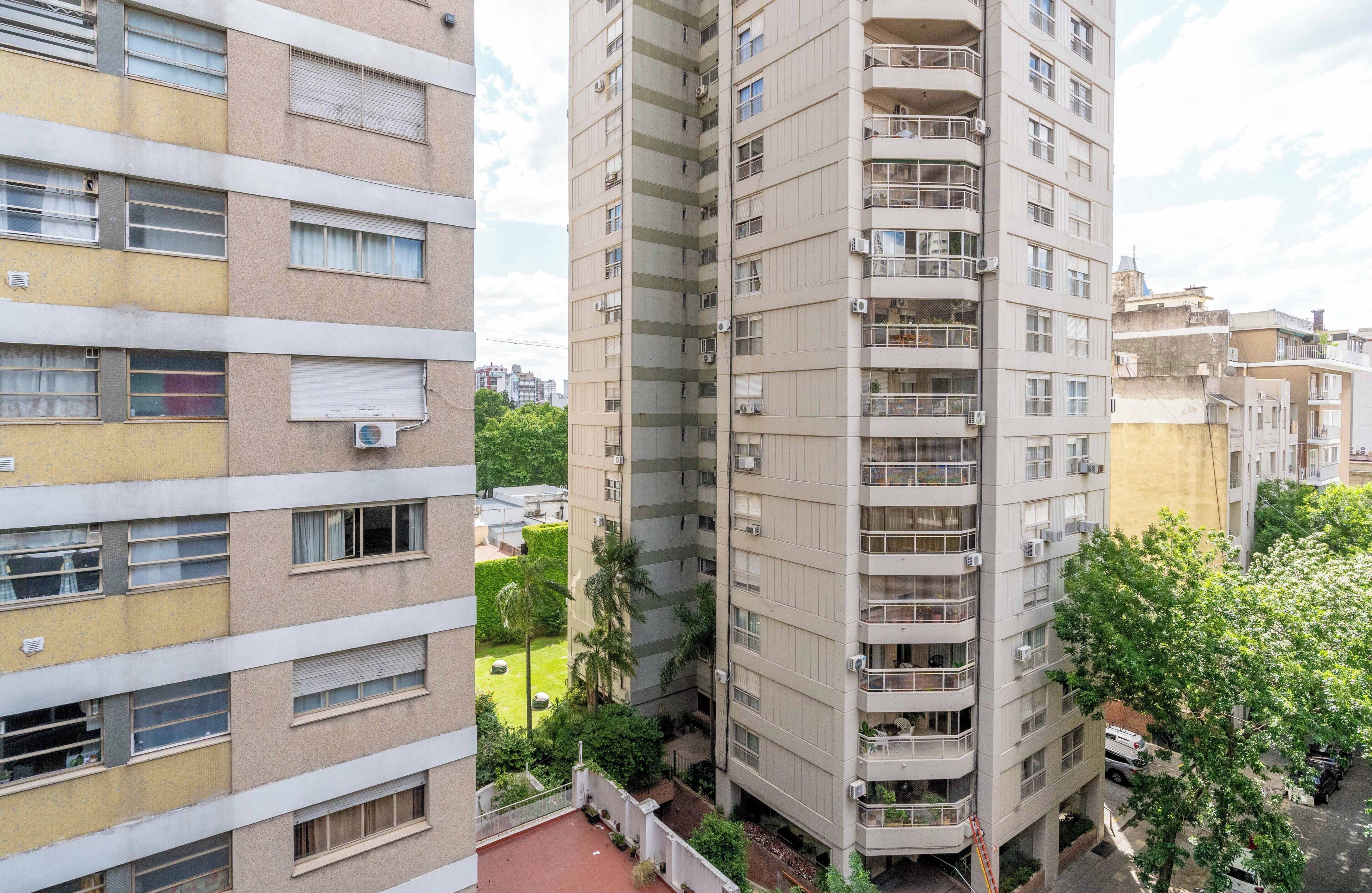 Un edificio residenziale a più piani con balconi, condizionatori e un cortile con vegetazione.