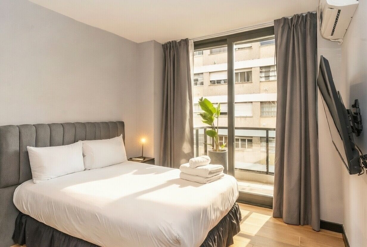 Una camera d'albergo con un letto, una pianta in vaso, una finestra con tende e un condizionatore d'aria a parete.