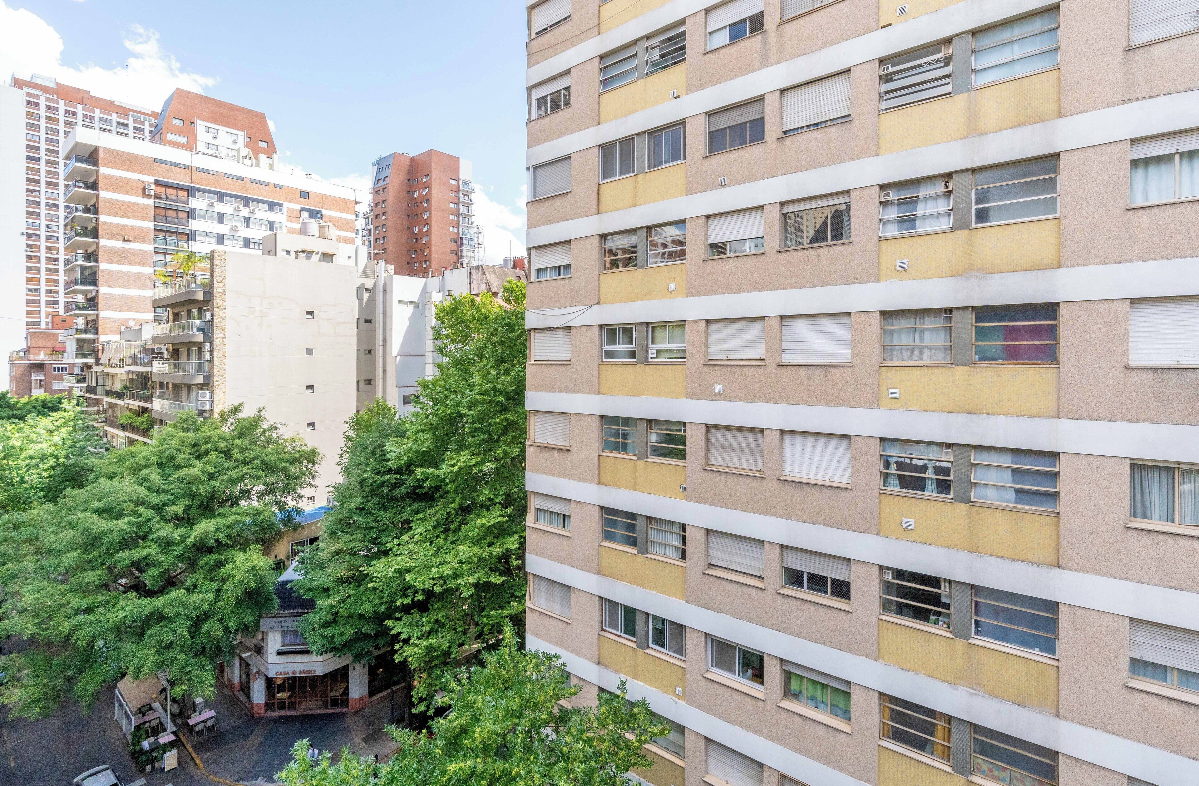 Un edificio residencial de varios pisos con balcones, una zona comercial en la planta baja y zonas verdes circundantes.