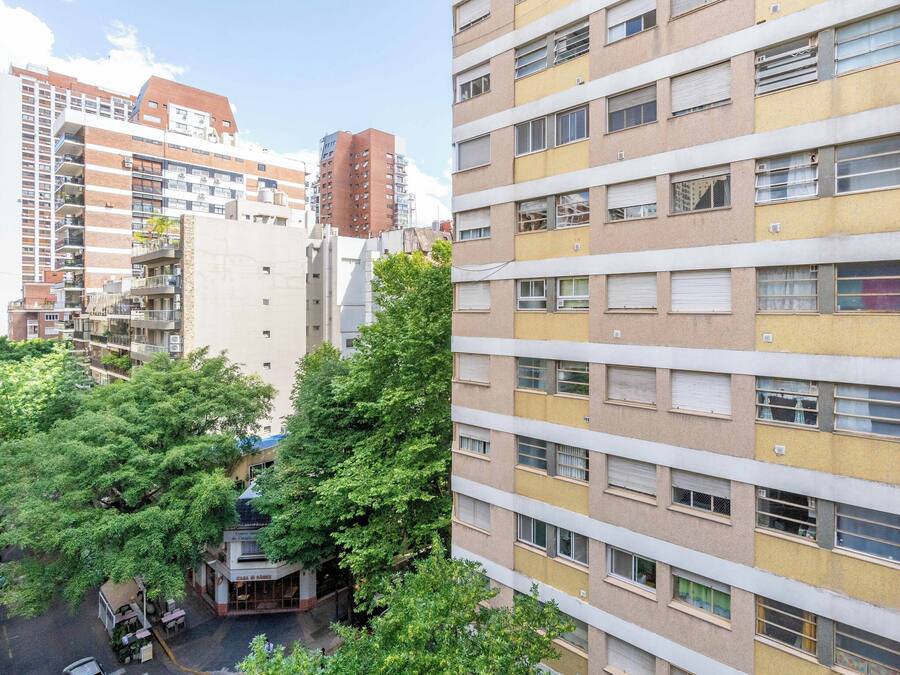Un edificio residencial de varios pisos con balcones, una zona comercial en la planta baja y zonas verdes circundantes.