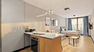 A modern kitchen with a central island, a dining area with a sofa, and a bedroom with a bed and curtains.