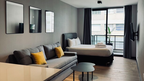 Ein modernes Hotelzimmer mit einer Couch, einem Bett, einem kleinen Tisch und einem großen Fenster mit Blick auf die Stadt.