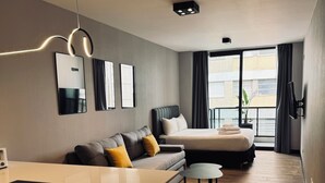 Ein modernes Hotelzimmer mit einer Sitzecke, einem Bett, einem kleinen Tisch und Blick auf die Stadt durch große Fenster.