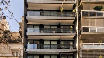 A multi-story building with balconies, a car parked in front, and a clear sky.