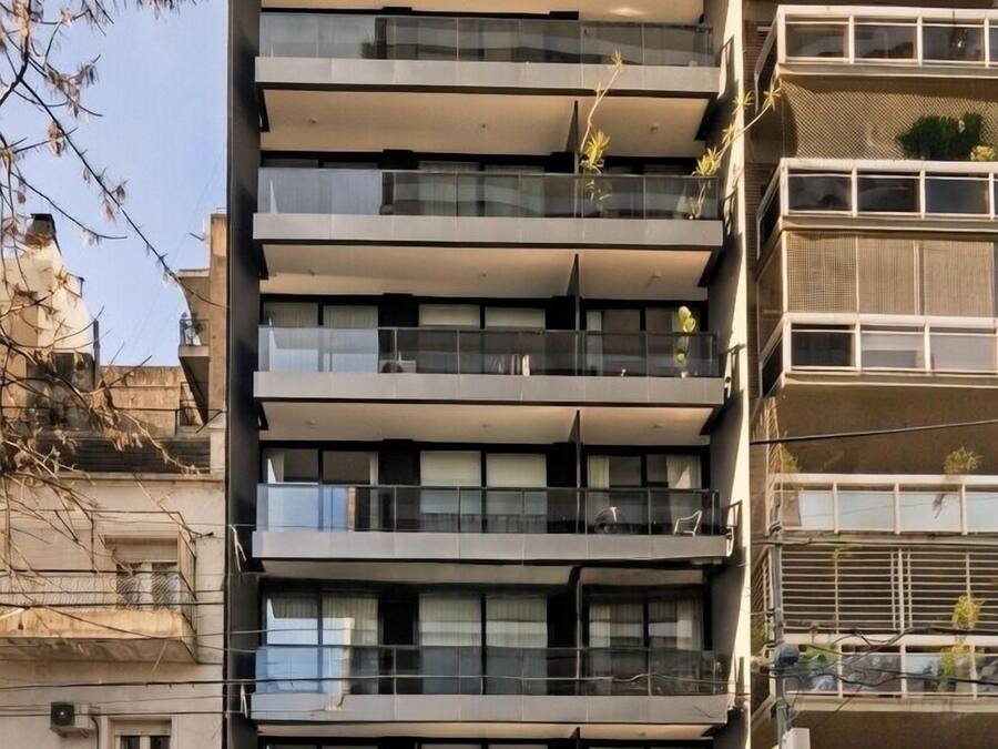 A multi-story building with balconies, a car parked in front, and a clear sky.