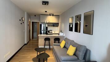 A modern living room with a grey sofa, two small tables, and a black side table with a remote control.