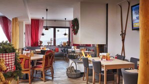 Un coin repas chaleureux avec des tables et des chaises en bois, une cheminée et une vue sur le paysage enneigé.