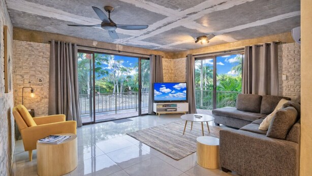 Un salón amplio con un televisor de pantalla plana grande, asientos cómodos y un balcón con vistas a zonas verdes.