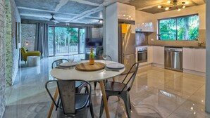 Una cocina moderna con electrodomésticos de acero inoxidable, un comedor con mesa redonda y vistas a zonas verdes a través de amplios ventanales.