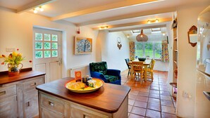 A kitchen with a wooden countertop, a dining area with a table and chairs, and a view of the garden through a window. - Porthcothan Mill Cottage (Porthcothan Bay)