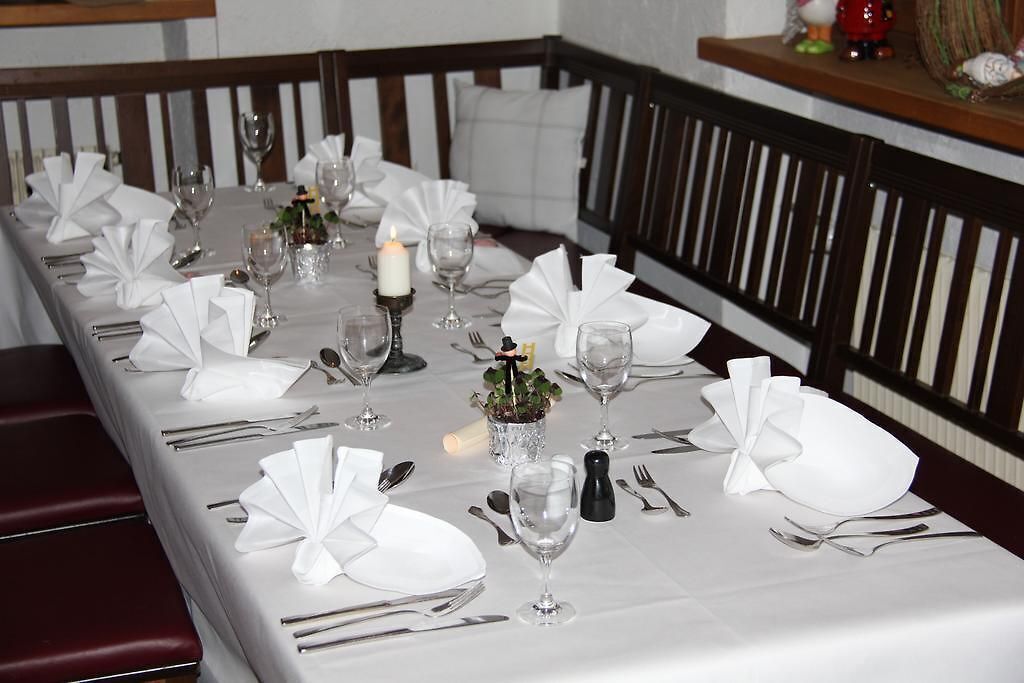 Una larga mesa de comedor dispuesta con manteles blancos, servilletas dobladas y copas de vino.