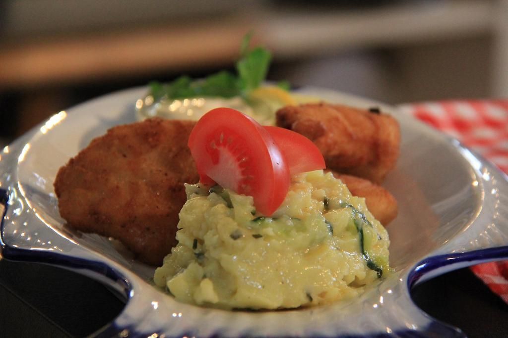 Un piatto con due cotolette e purè di patate guarnito con una fetta di pomodoro.