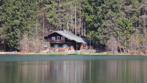 A cabin by a lake surrounded by dense forest. - Berggasthof Willy Merkl (Schliersee)