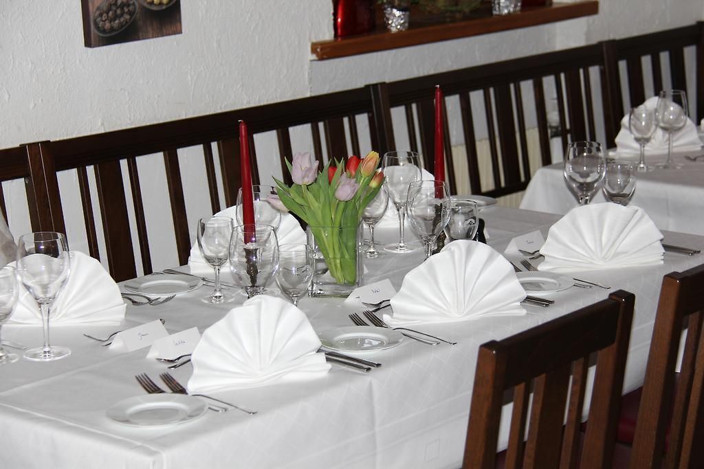 Ein Restaurantambiente mit gedeckten Tischen, weißen Tischdecken, gefalteten Servietten und einem Strauß Tulpen.