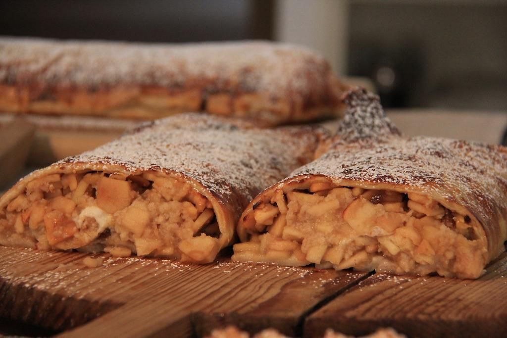 A loaf of bread with a dusting of powdered sugar, sliced and placed on a wooden surface.