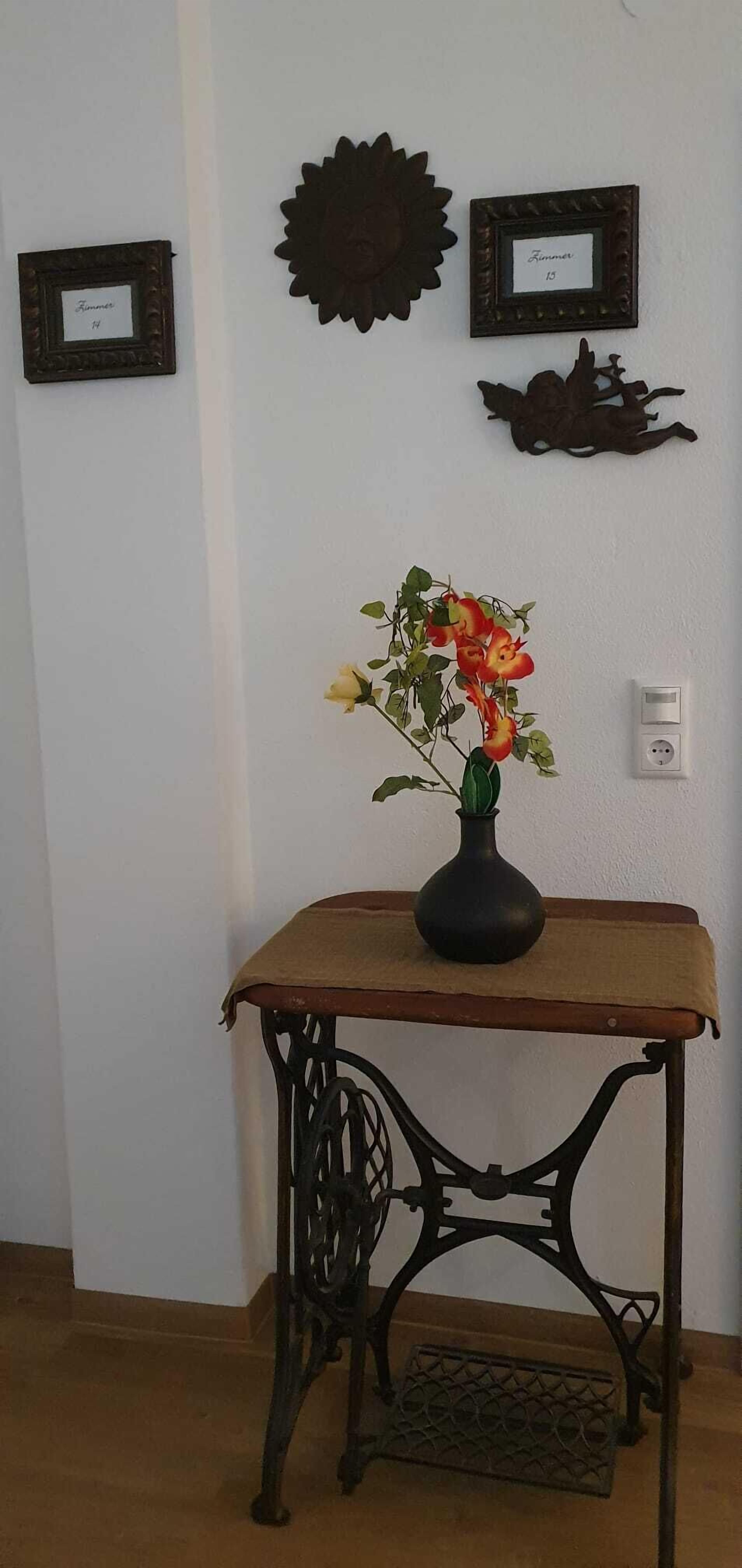 A room with a table, a vase with flowers, and two wall-mounted decorations.