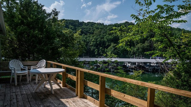 A wooden deck with a table and chairs, overlooking a dock and a body of water surrounded by dense greenery. - Charming 2-bedroom Duplex in Albany, KY on Dale Hollow Lake with Slip #20 (Albany)