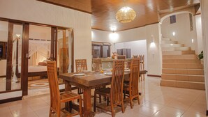 A dining area with a wooden table and chairs, a chandelier, and a staircase leading to an upper level. - Coco Villa (Ubud)
