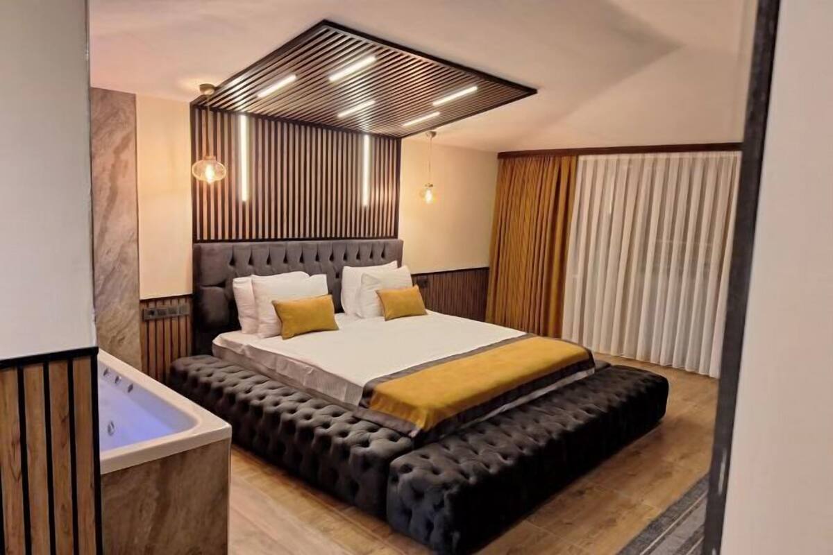 A modern bedroom with a large bed, a built-in bench, and a small bathroom.