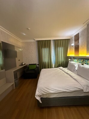 Ett modernt hotellrum med en stor säng, en sittgrupp med soffa och fåtölj, en platt-TV och en dekorativ väggpanel.