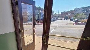 A view through a wooden door with a metal handle, leading to a street with parked cars and buildings. - The Loft on Winter - Downtown Adrian (Adrian)